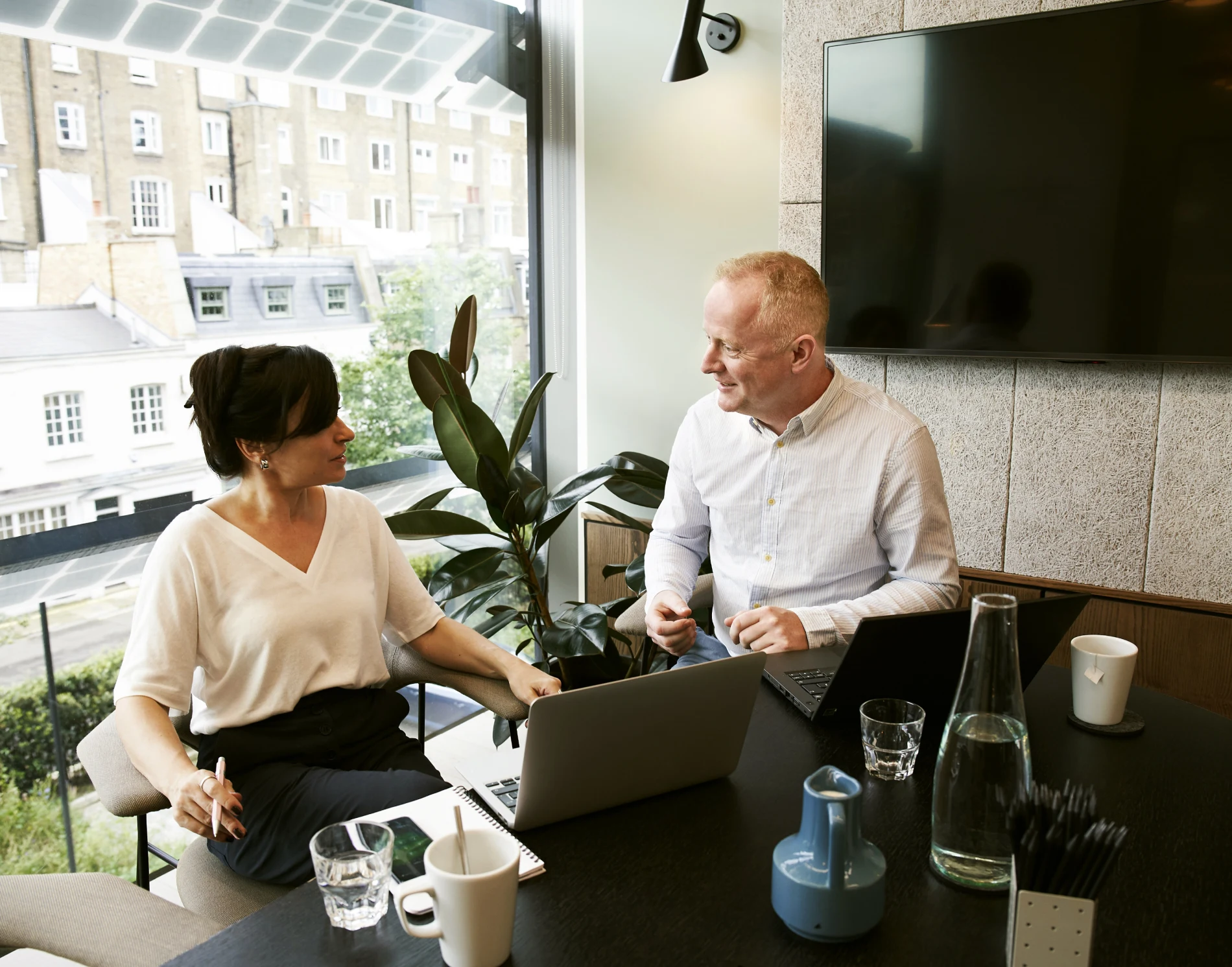 Two people sitting at a table with laptops.